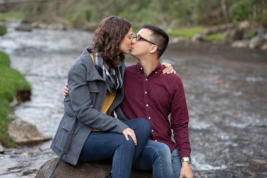 Engagement portrait of couple sitting on rock in river at Roan Mountain